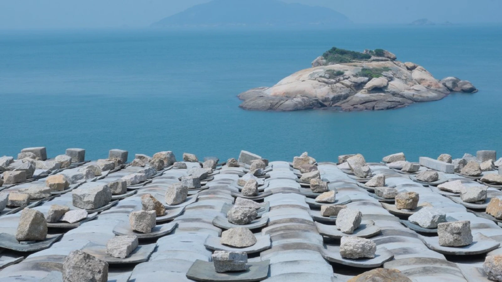 Stone-weighted tile roofs overlooking the sea and a small rocky island in the Matsu Islands